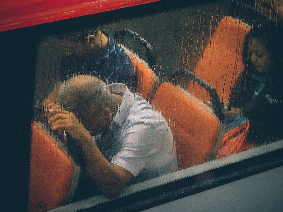 Man on bus, head in hands against seat in front of him, despair
