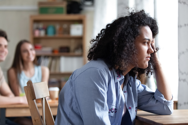 Woman sitting separated from peers, head on hand, looks sad.