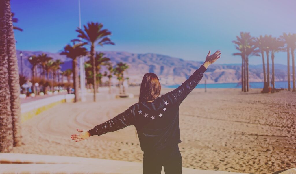 Woman with arms outstretched on a beach.