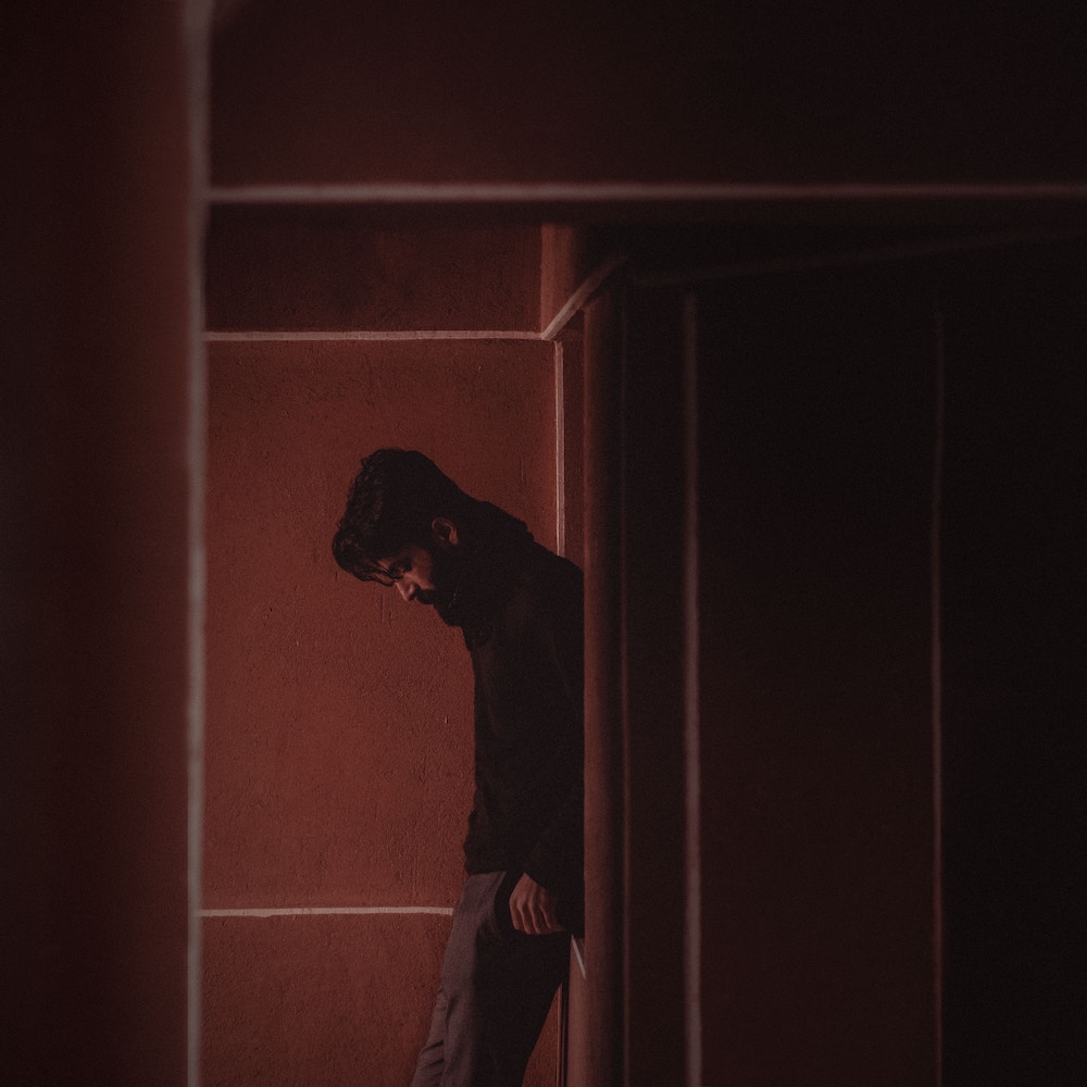 Side view of young man looking down, in dim light.