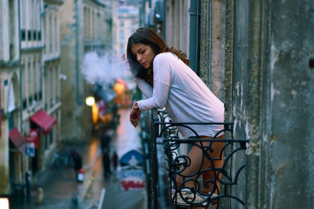 Life Goes On: Reflections on 2019 Woman standing on balcony, smoking, overlooking the street