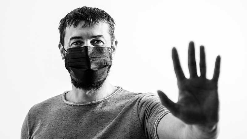 Man with mask holds hand out in front of him.