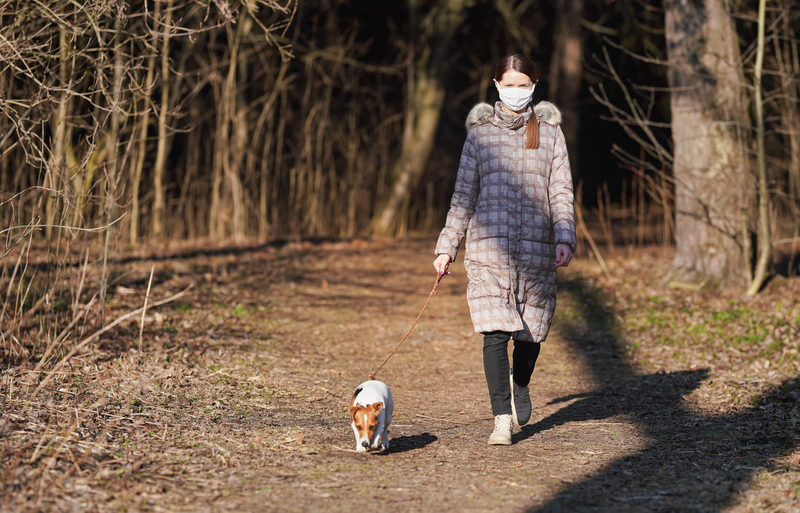 Woman walking dog and wearing medical mask.