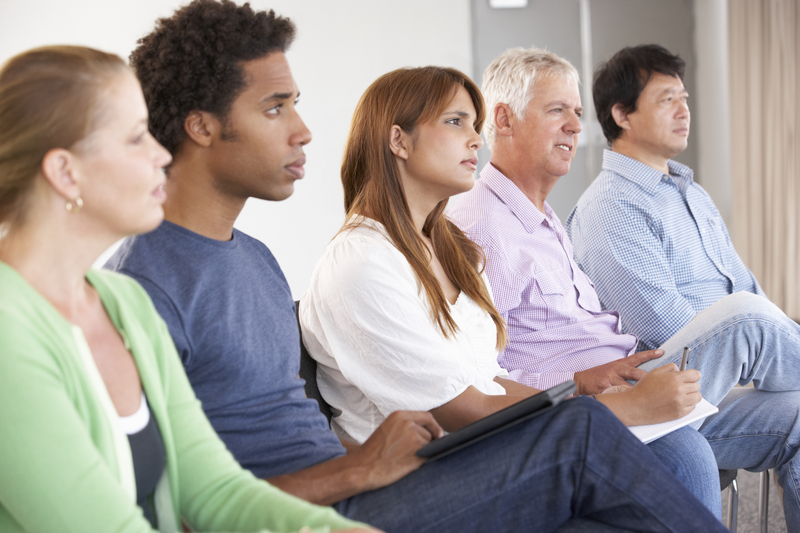 Group of people sitting in chairs in a row, watching someone, AA meeting