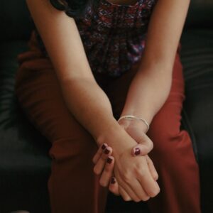 Person's arms, hands clasped and resting on legs.