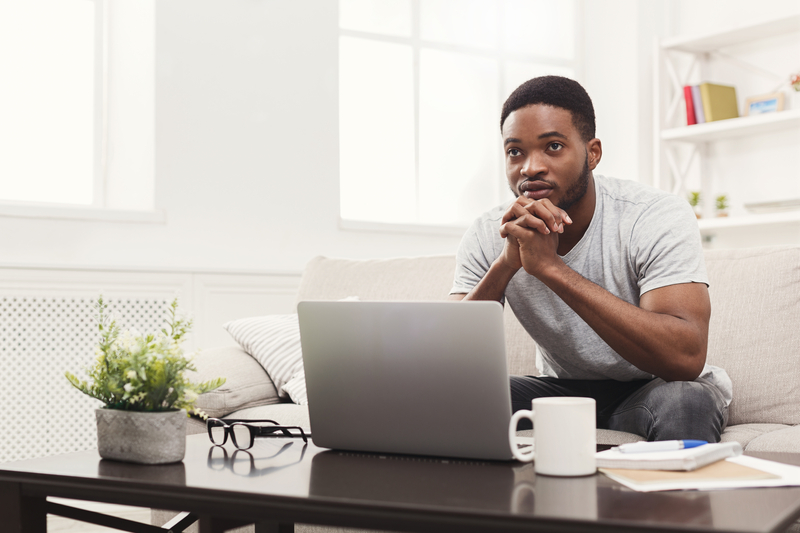 Young man on couch looking at laptop, looks thoughtful