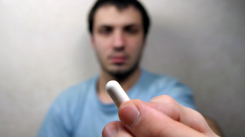 Blurry image of man holding pill which is in focus.