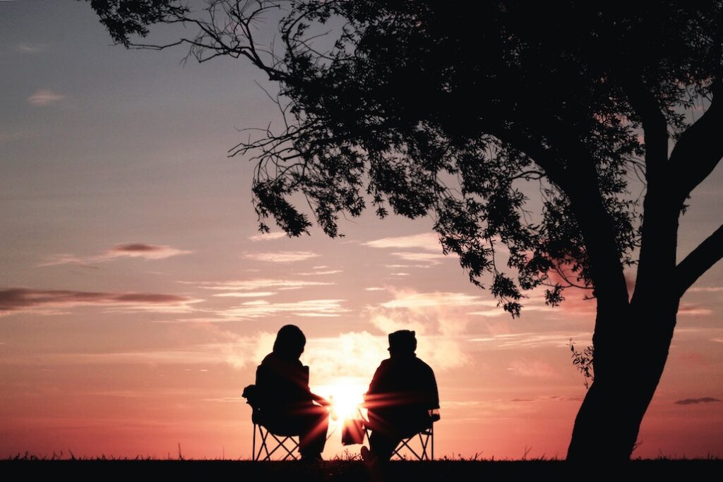 What Is a Sober Coach? Two people sitting outside under a tree, silhouetted by setting sun