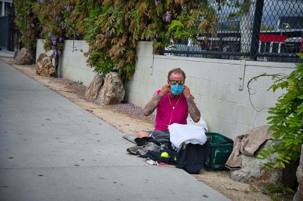 Pandemic Presents New Hurdles, and Hope, for People Struggling with Addiction Homeless man sits on ground wearing mask.