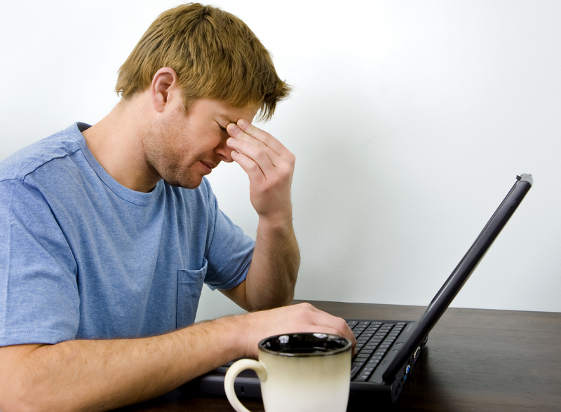 Unhappy man on his laptop, fingers at bridge of nose.