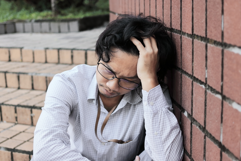 Man, disappointed, sits on steps and leans against brick wall.
