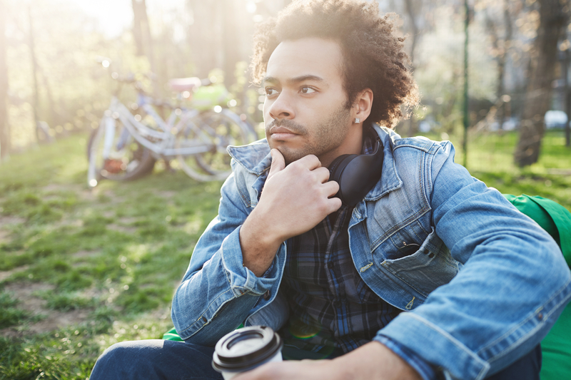 Thoughtful man touching beard, outside, with coffee cup