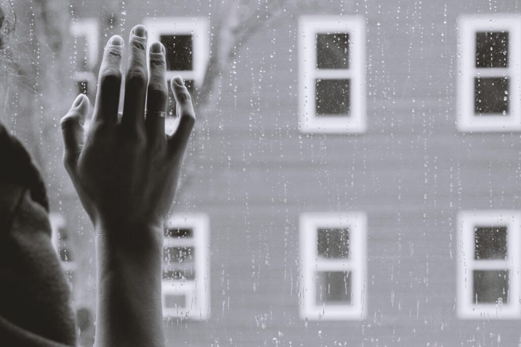 Black and white image, hand at window, rain and building outside.