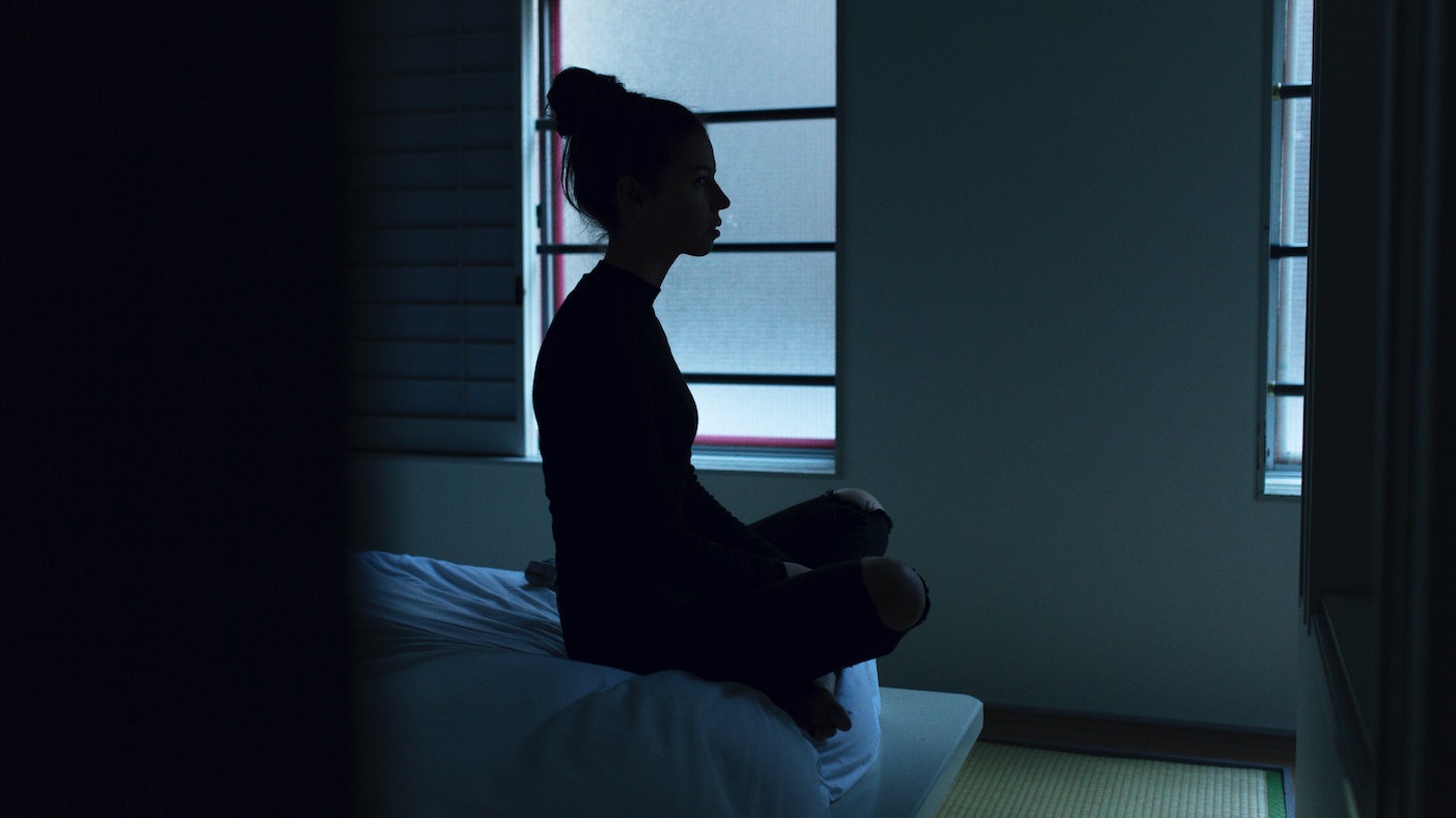 Silhouette of woman cross-legged on bed in darkness