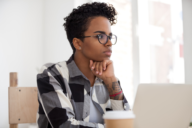 Woman stares thoughtfully over laptop computer