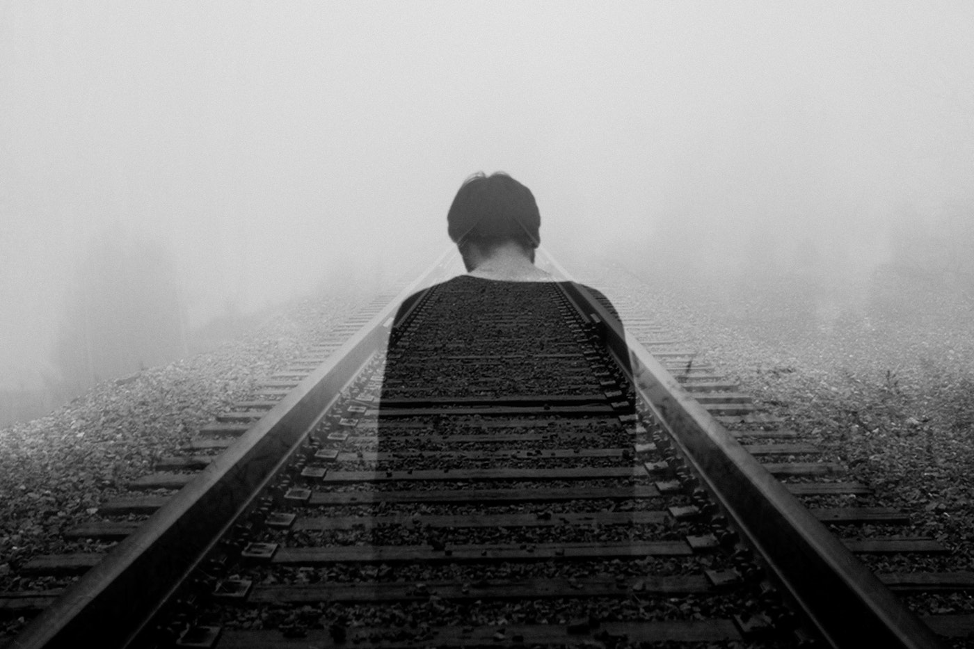 Black and white image of man from back, semi-transparent, standing on railroad tracks