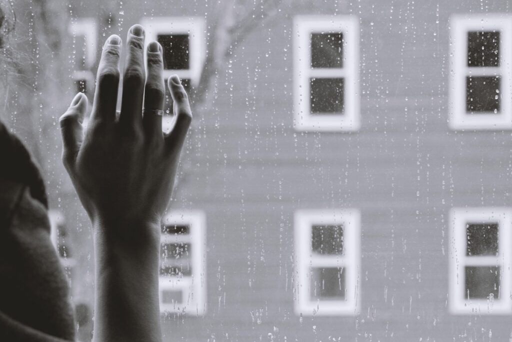 Failing Black and white image of hand against a window, outside is six windows, the side of a building or house