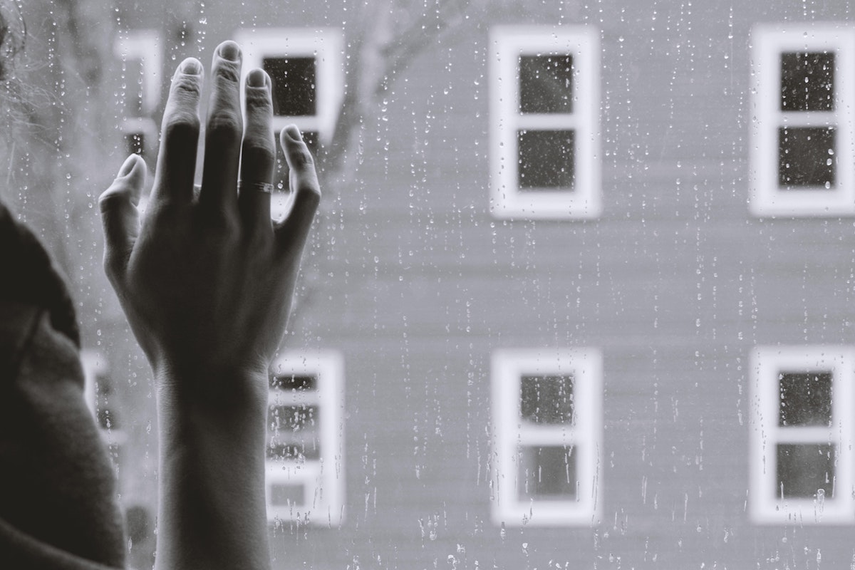 Black and white image of hand against a window, outside is six windows, the side of a building or house