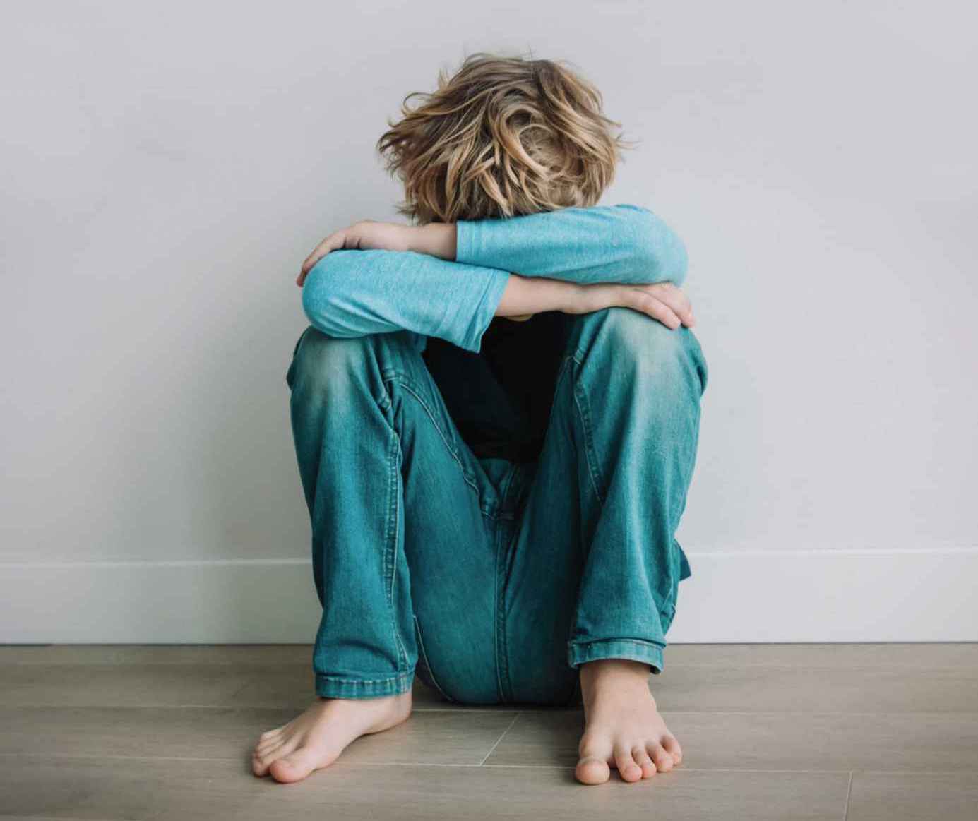 A child sitting on the floor with knees up and resting arms on knees, head bowed into arms.