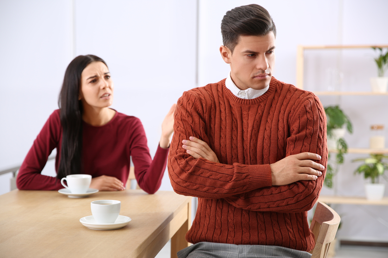 couple sitting at table, woman arguing with silent man who is turned away.