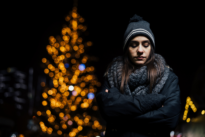 Woman in front of lit up tree, looks sad and lonely