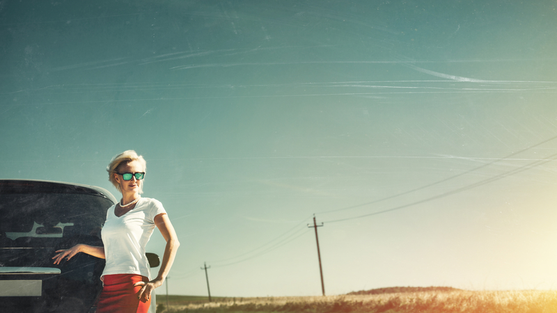 Woman standing by car on rural highway, hand on hip, looking into distance