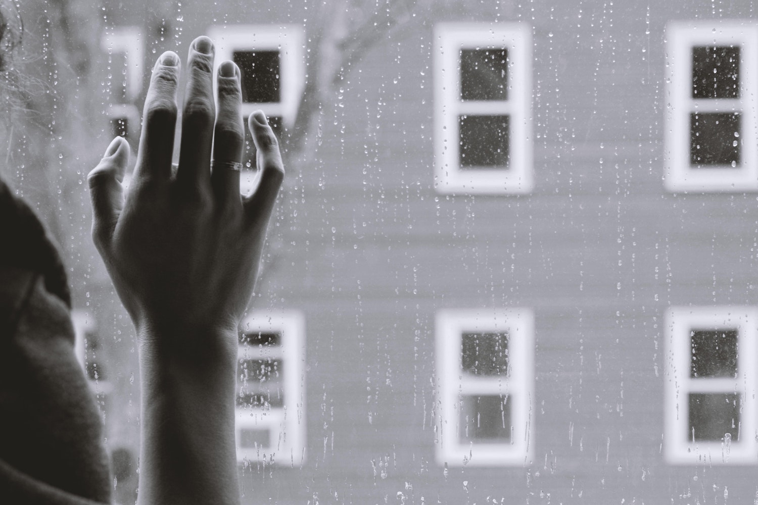 A woman's hand against a rain-streaked window