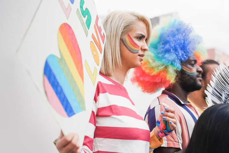 Gay pride parade, focus on blonde woman holding pride poster with rainbow on face
