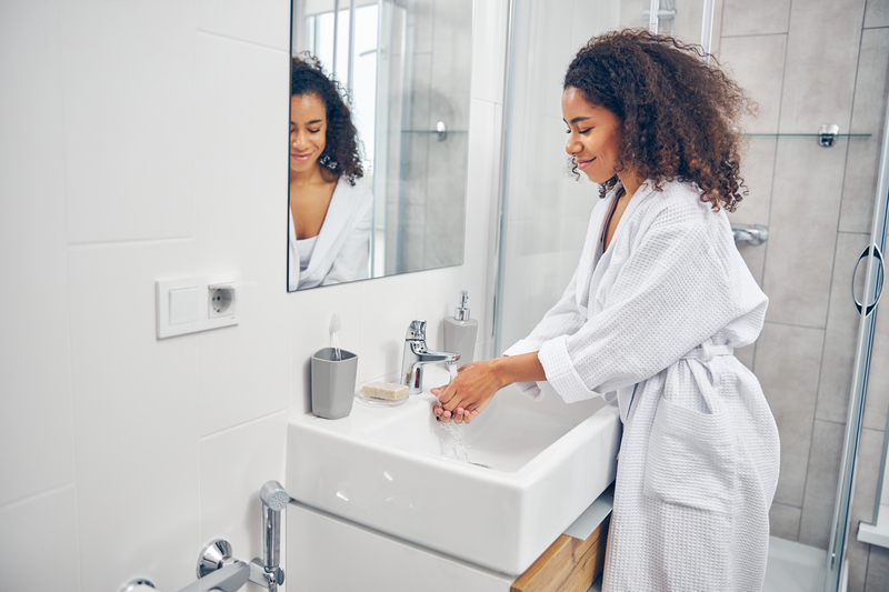 Woman in white robe smiles as she washes her hands.