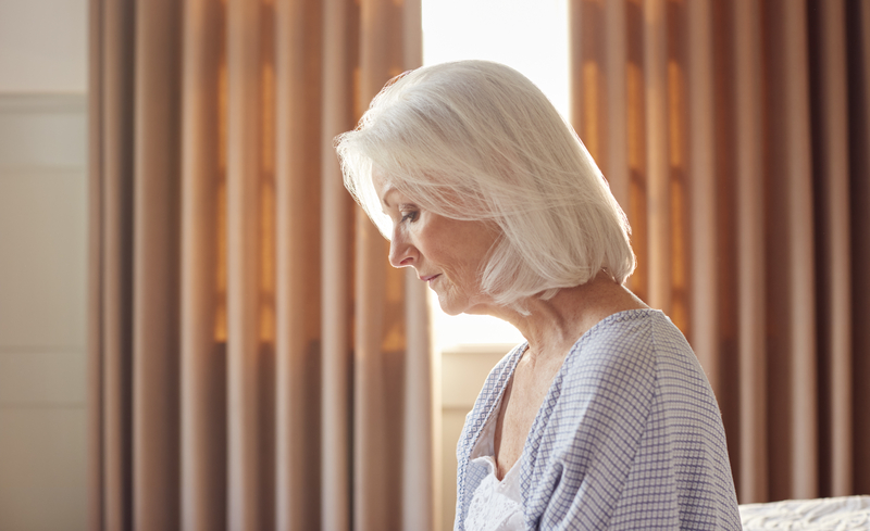 Woman sits on edge of bed, sad