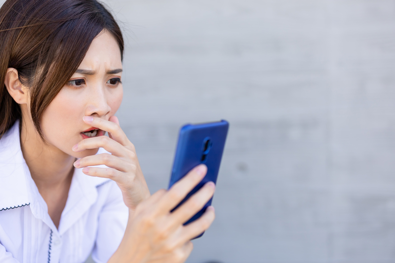 Woman looks at mobile phone with shocked expression