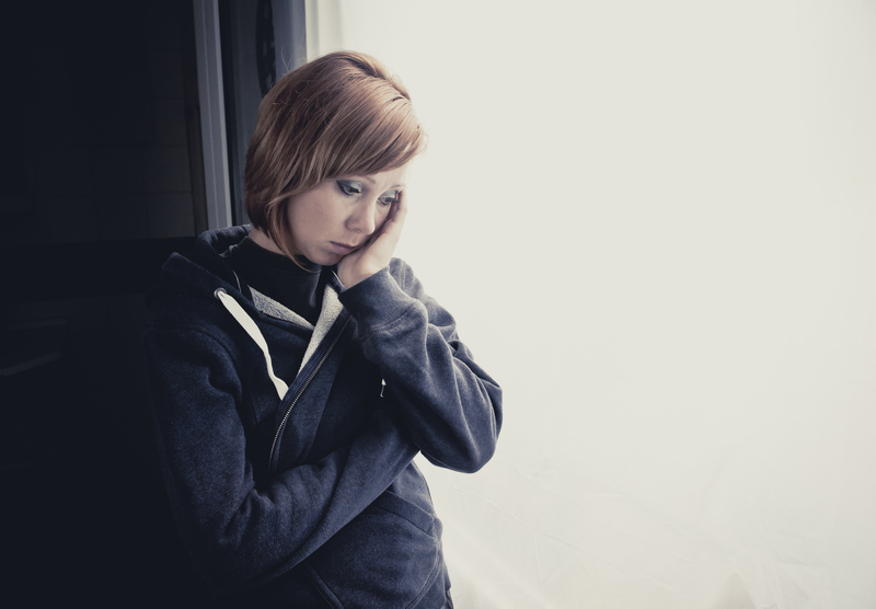 Woman looks sad, stands alone, head against hand