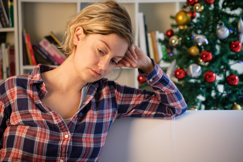 Sad woman on couch in front of Christmas tree