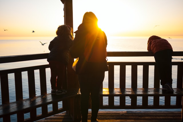 Mother and two children on a pier overlooking the sea, outlined by sunset