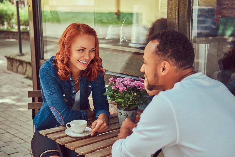 Couple drinking coffee outdoors on a date, smiling