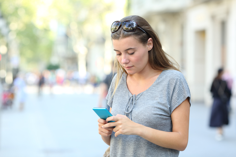 Teenage girl stands outside looking at mobile phone